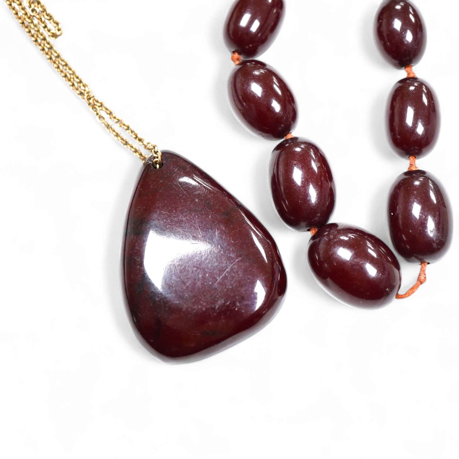 A cherry bakelite 'amber' necklace and pendant, comprising: a necklace composed of cherry-coloured bakelite beads measuring approximately 10 - 26mm, length 90cm; and a drop-shaped pendant, length 5.7cm, on a gilt metal c